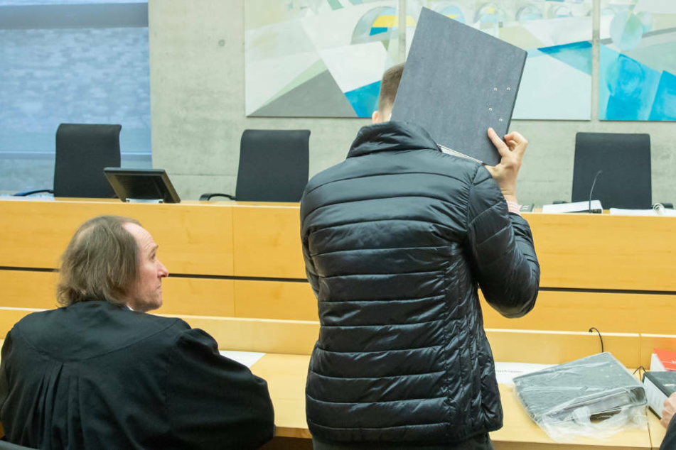 Der wegen Missbrauchs von Kindern angeklagter Logopäde trifft zum Prozessbeginn im Sitzungssaal im Landgericht ein und hält sich einen Aktenordner vor das Gesicht.
