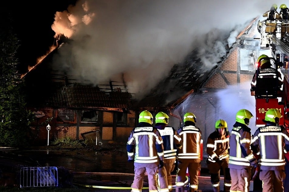 Einsatzkräfte der Feuerwehr stehen vor dem brennenden Gebäude in Geesthacht.