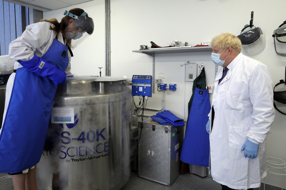 Großbritannien, Oxford: Boris Johnson (l), Premierminister von Großbritannien, trägt Schutzkleidung und Maske, während Professorin Kate Ewer ihm bei seinem Besuch im Jenner Institute Proben zeigt.