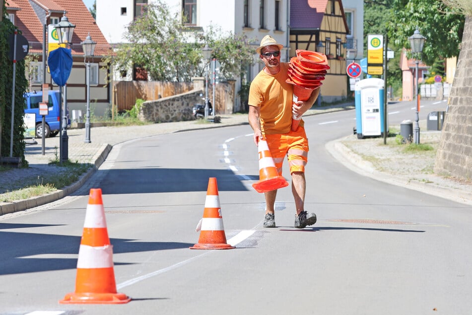 Frisch saniert strahlt der Asphalt der Pillnitzer Landstraße. Ein Arbeiter sammelte nach dem Trocknen der Fahrbahnmarkierung am Mittwoch die abgestellten Leitkegel wieder ein.