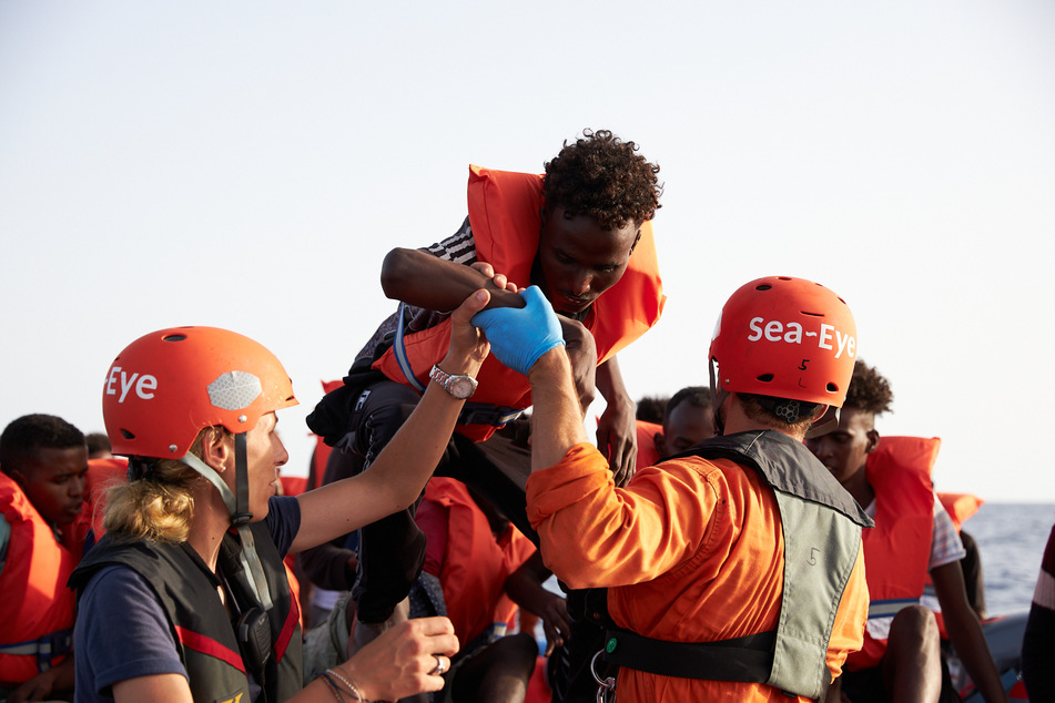 Die von der Seenotrettungsorganisation Sea-Eye herausgegebene Aufnahme zeigt Seenotretter, die Flüchtlinge im Mittelmeer von einem Schlauchboot evakuieren.
