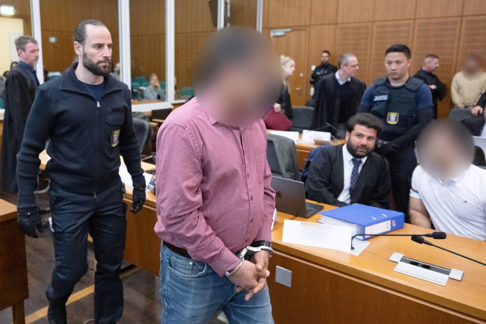 Der Hauptangeklagte, der hier in Handschelle in den Gerichtssaal geführt wird, soll im August 2024 an Gleis 9 des Frankfurter Hauptbahnhofs einen 27 Jahre alten Mann erschossen haben.