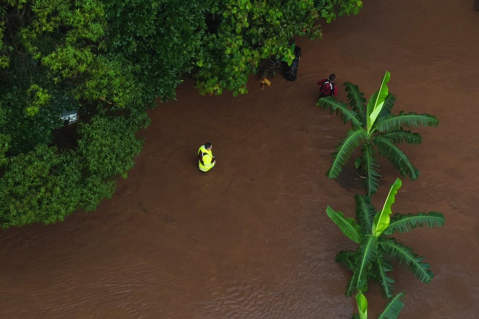 People wearing reflective vests walk in floodwater as evacuation efforts take place on the Hawaiian island of Oahu on March 20, 2026.