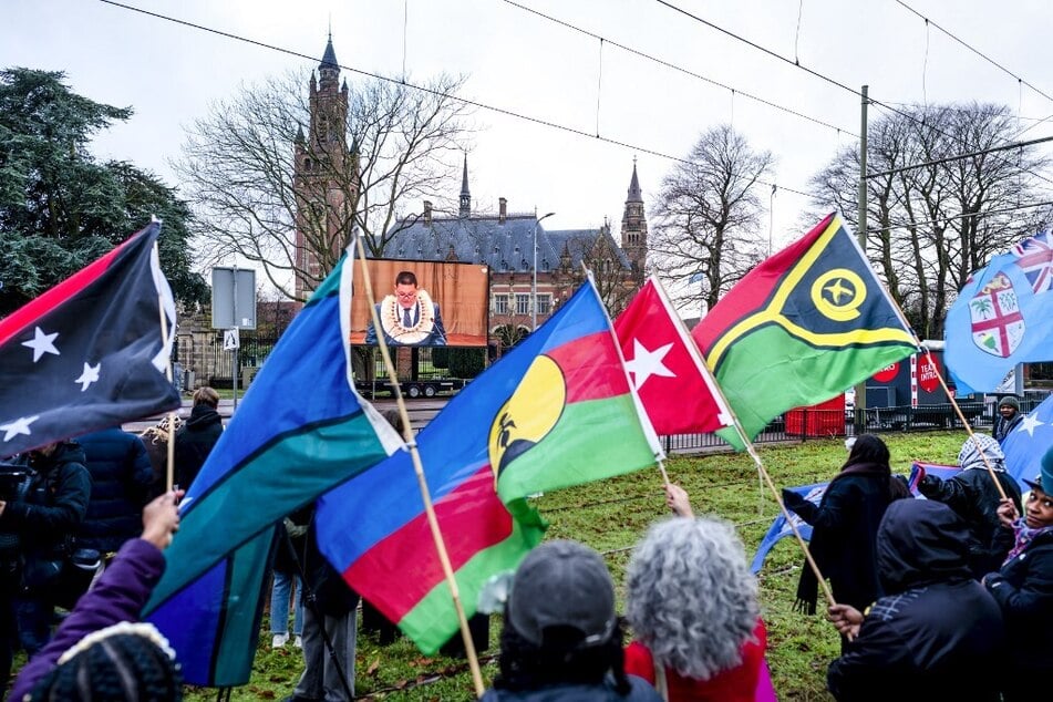 Climate activists wave flags as they demonstrate in front of the International Court of Justice in The Hague, Netherlands.