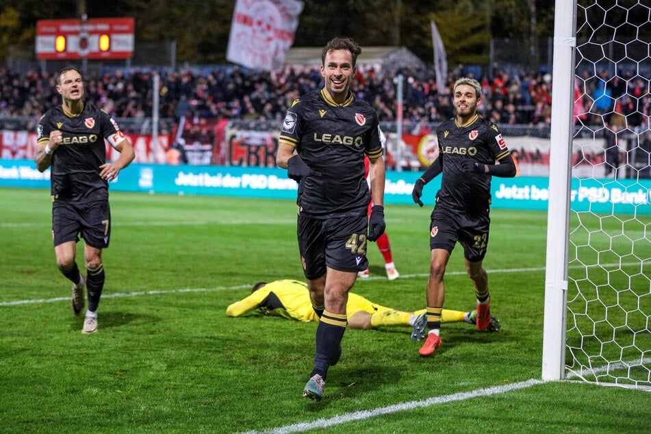 Kölns Keeper Dudu (in Gelb am Boden) patzt, Cottbus' Maximilian Pronichev (v.) sagt Danke.