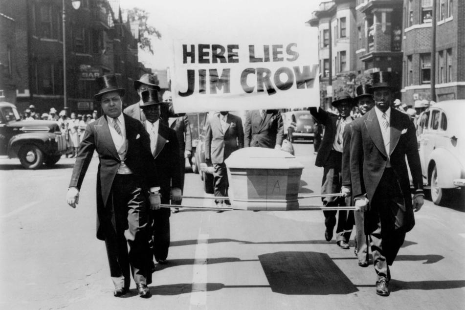 Six African-American men in top haps and tails carry a coffin with the sign "Here Lies Jim Crow" during a 1944 Parade for Victory in Detroit, Michigan.