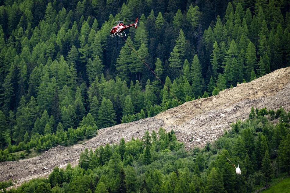 Ein Helikopter der Air Zermatt fliegt über einer Alp oberhalb von Wiler mit Eisblöcken und Felsbrocken, die sich vom Birchgletscher oberhalb des Dorfes Blatten ansammeln.