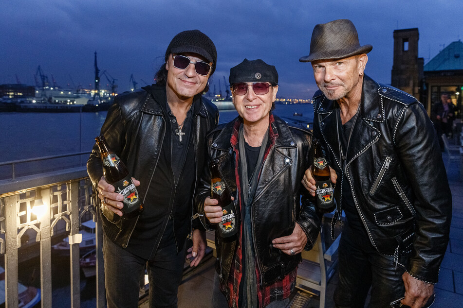 Die Musiker der Rockgruppe Scorpions Matthias Jabs (l-r), Klaus Meine und Rudolf Schenker präsentieren ein Bier, das ihren Namen trägt - ganz ohne Maske, dafür aber mit breitem Grinsen.