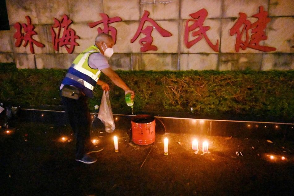 A worker on Tuesday douses candles left outside the Zhuhai Sports Centre, a day after a car rammed through the site killing dozens in Zhuhai, in south China's Guangdong province.