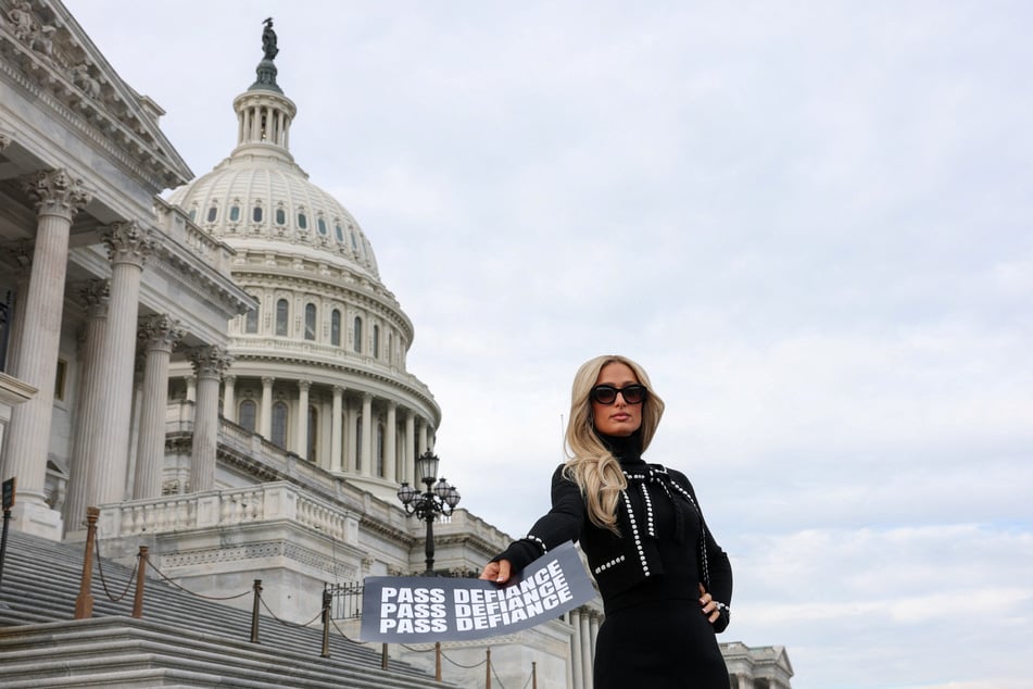 Paris Hilton poses on the Capitol steps with a sign reading "Pass DEFIANCE" on January 22, 2026.