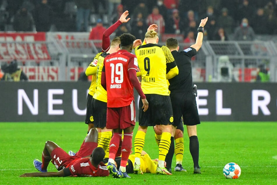 Dortmunds Julian Brandt (u.r.) und Münchens Dayot Upamecano (u.l.) liegen verletzt auf dem Boden, Mannschaftskollegen rufen um Hilfe.