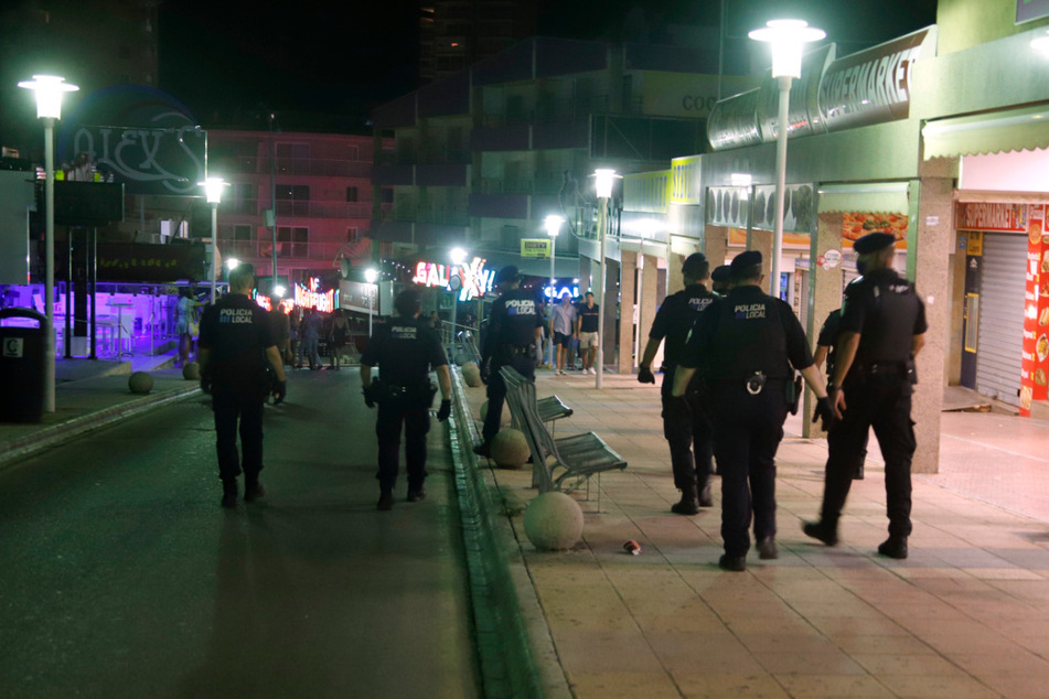 Polizeibeamte mit Mundschutz patrouillieren nachts auf der Straße Punta Ballena im Touristenort Magaluf.