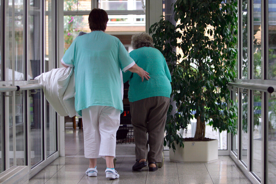 Eine Altenpflegerin geht mit einer Seniorin durch einen Flur in einem Altenheim.