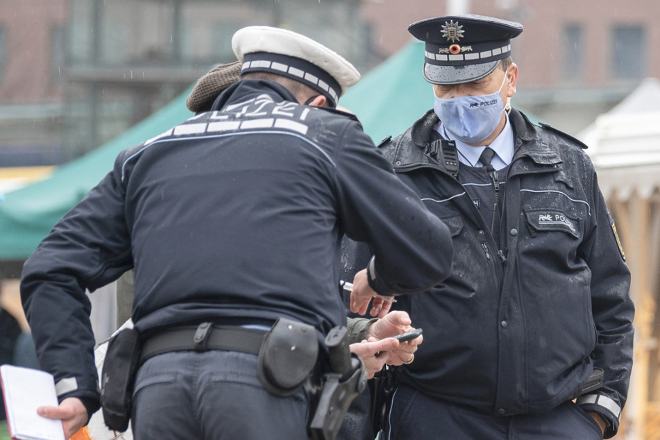 Polizeibeamte kontrollieren während einer Schwerpunktkontrolle zur Einhaltung der Corona-Maßnahmen auf einem Wochenmarkt einen Marktbesucher.