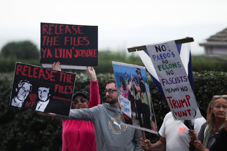People hold signs calling for the release of the Jeffrey Epstein files as Donald Trump's motorcade passes by on its way to Turnberry, Scotland, on July 25, 2025.