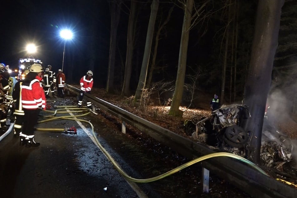 Einsatzkräfte der Feuerwehr löschen ein brennendes Auto im Wald. Für den Autofahrer kam jede Hilfe zu spät.