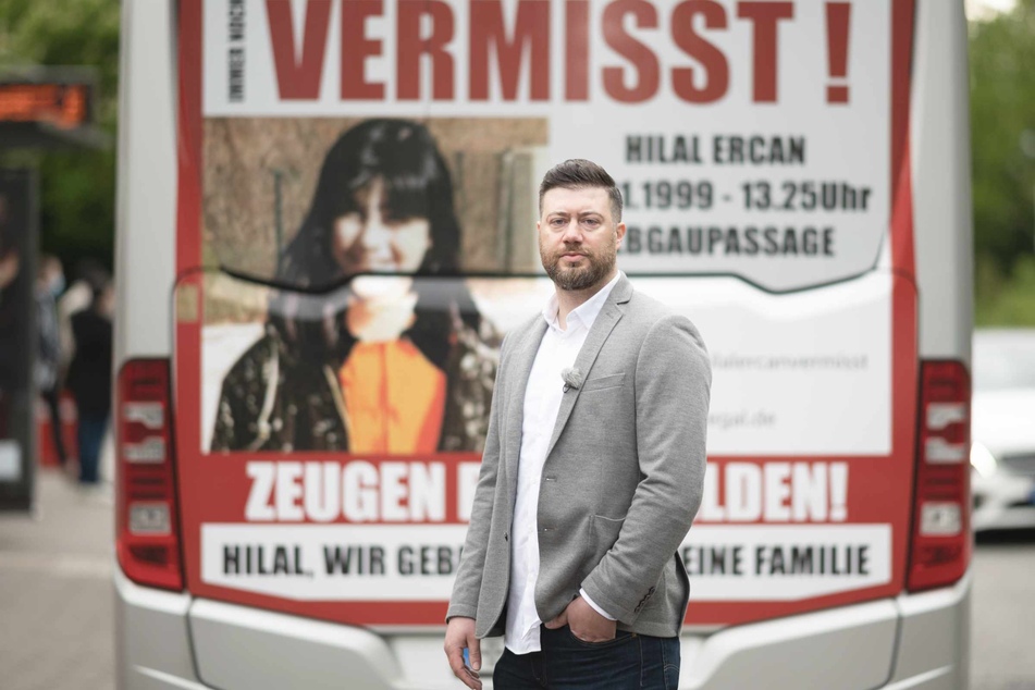 Abbas Ercan, Bruder der vermissten Hilal Ercan, steht vor einem Bus, der mit einem großflächigen Zeugenaufruf plakatiert ist.