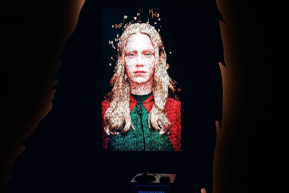 Eine KI-generierte Projektion von Kraka ist gleich dreimal in der Ausstellung vertreten. Über ein Mikrofon können Besuchende direkt mit ihr sprechen. Sie antwortet mit poetischen, variierenden Texten über das Leben der Wikinger, aber auch über Brotbacken oder wie sie Hamburg findet.