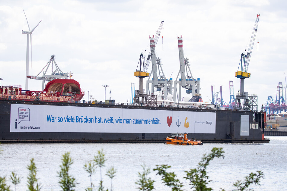 Ein großes Banner mit dem Hinweis auf ein Informationsportal zur Corona-Pandemie hängt am Schwimmdock 11 der Hamburger Werft Blohm+Voss.