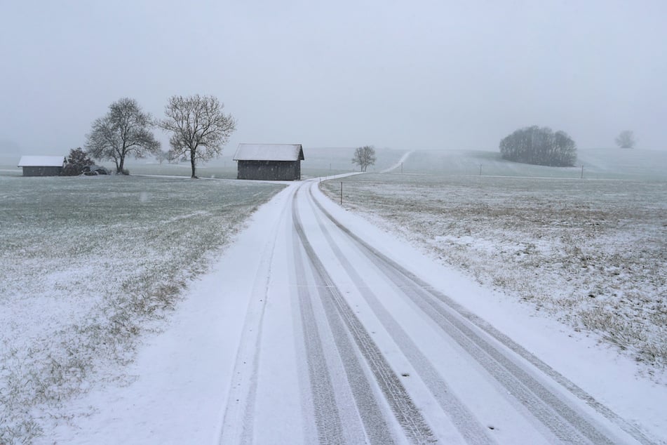Im Schneetreiben führt eine Landstraße durch die Allgäuer Landschaft.