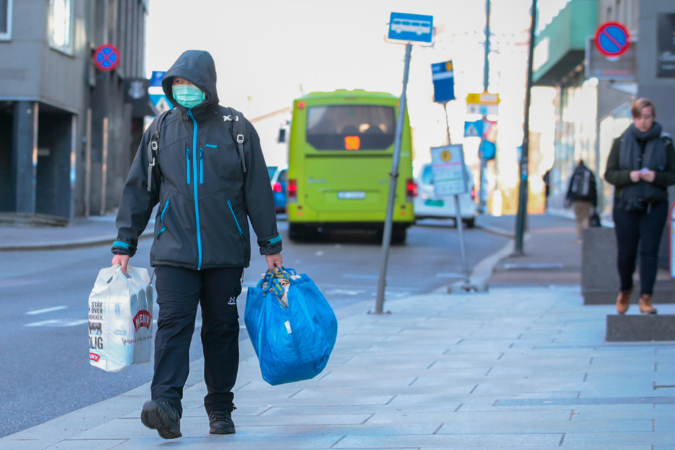 Ein Mann mit einem Mundschutz läuft mit Einkaufstaschen durch die Straßen von Oslo.