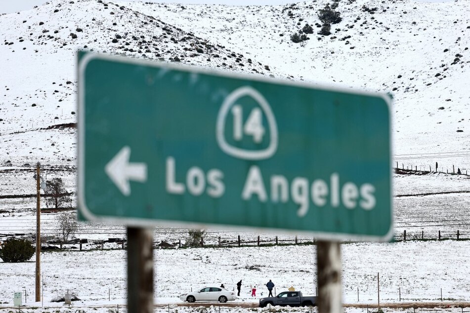 People walk in the snow near a freeway sign pointing to the city of Los Angeles near Acton, California.