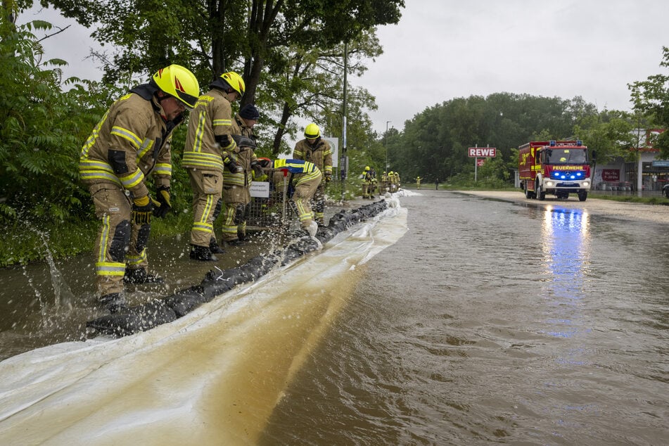 Feuerwehrleute arbeiten an einer von der Günz überfluteten Straße in Ichenhausen, um das Wasser aus der Stadt fernzuhalten.