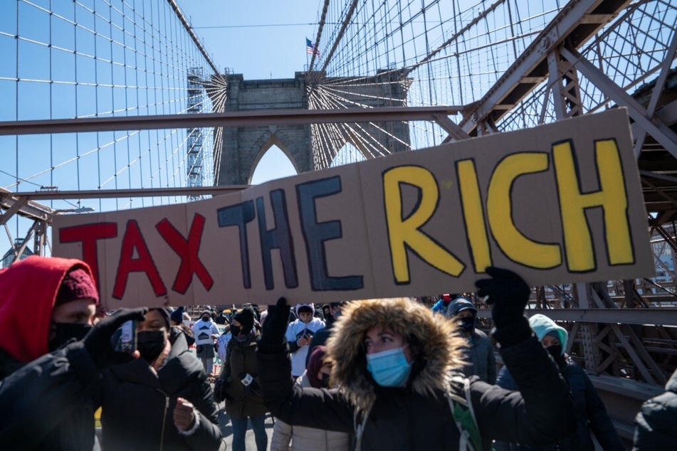 Protestors march across New York City's Brooklyn Bridge holding a sign to "tax the rich."