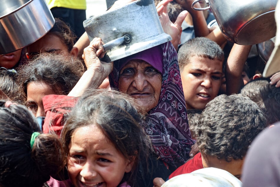 An elderly Palestinian woman waits with children to receive food from a charity kitchen in Khan Younis in the southern Gaza Strip on August 21, 2025.