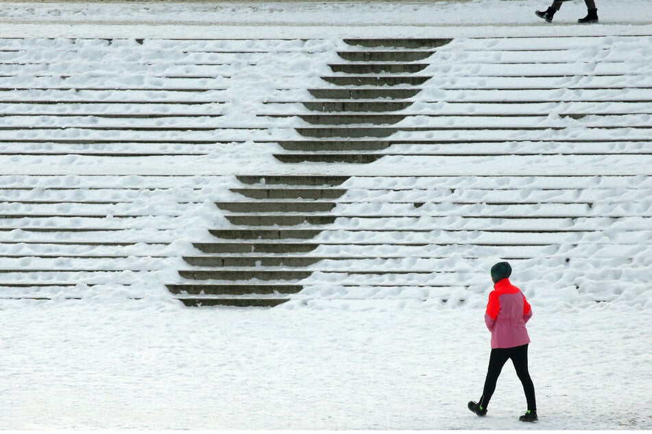 Eine Frau läuft bei Temperaturen um Minus sechs Grad Celsius im Bezirk Mitte an den verschneiten Treppen zum Reichstagsgebäude entlang.