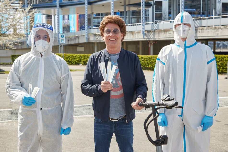 Atze Schröder (55, M.) steht während eines Pressetermins zusammen mit Testern Cesar Catute (l.) und Henri Hausherr am Drive-In-Testzentrum auf dem Parkplatz der Barclaycard Arena.