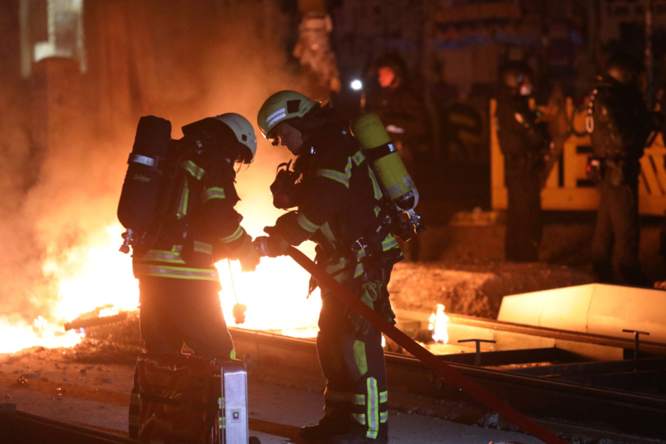 Feuerwehrleute haben sich zur brennenden Barrikade vorgekämpft und beginnen mit den Löscharbeiten.