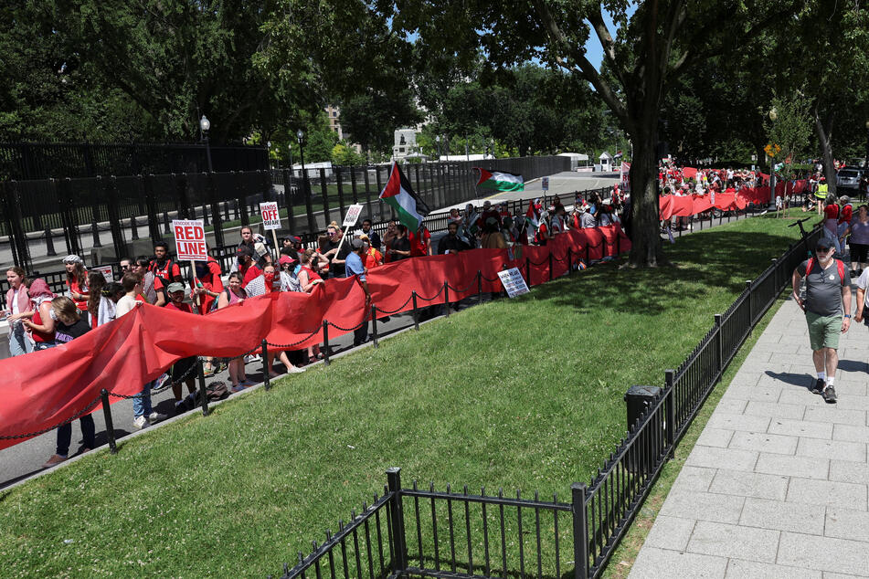 Hundreds of protesters surround the White House perimeter with a red banner symbolizing President Biden's supposed "red line" about Israel going into Gaza's Rafah.