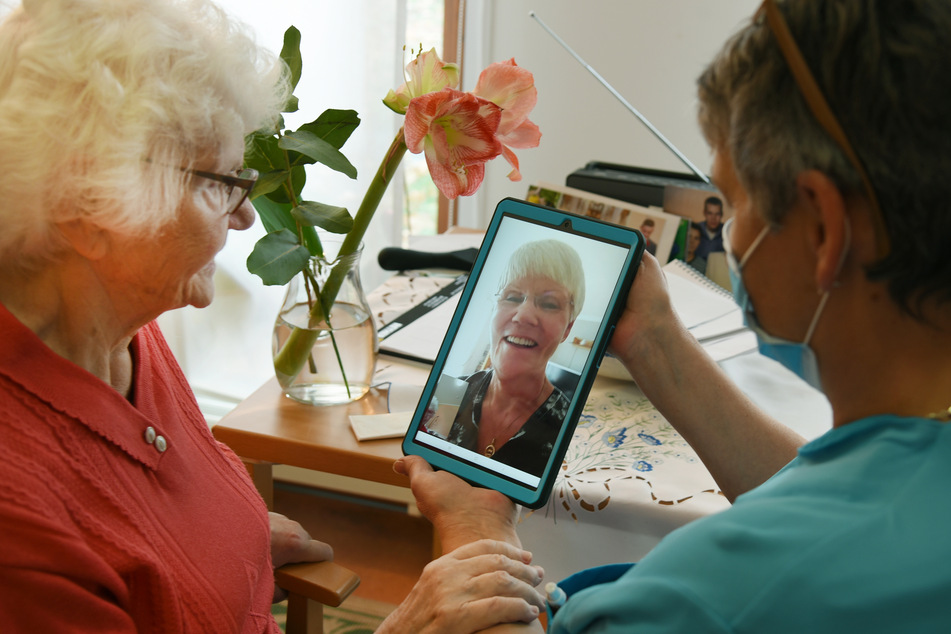 Im Haus der Generationen der Paul-Riebeck-Stiftung in Halle/Saale hält die Pflegeassistentin Inge Schenk ein Tablett für die 91-jährige Heimbewohnerin Hildegard Zipfel in der Hand, deren Tochter per Videotelefonie zugeschaltet ist.