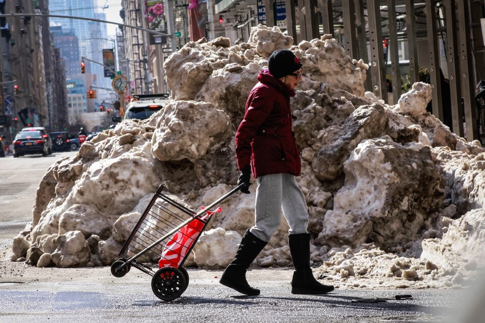 Snow piles cover the sidewalk as a person crosses the street in Midtown Manhattan in New York City on Sunday.