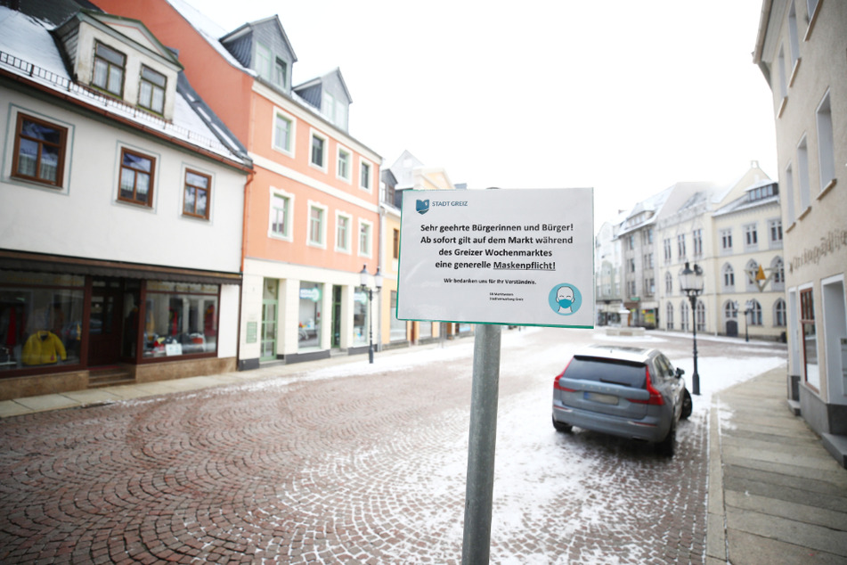 Ein Hinweisschild auf die Maskenpflicht steht am Marktplatz in der Innenstadt von Greiz. In Thüringen sind die Inzidenzzahlen im bundesweiten Vergleich weiter am höchsten.
