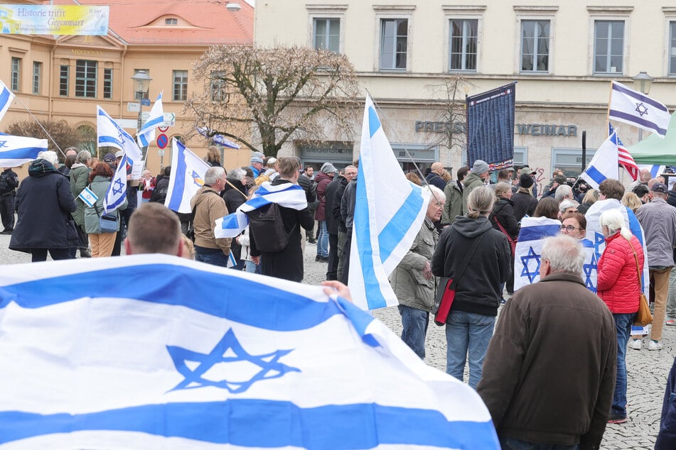 Teilnehmer mit der Flagge Israels stehen bei einer Kundgebung der Deutsch-Israelischen Gesellschaft gegen Propaganda in Buchenwald auf dem Goetheplatz.