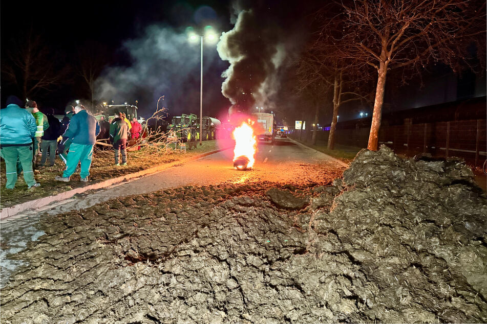 Protestteilnehmer blockieren mit Mist und brennenden Reifen eine Straße bei Magdeburg.