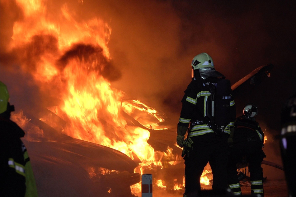 Feuerwehrleute kämpfen sich an die Feuersäule heran, die über den brennenden Autos steht.