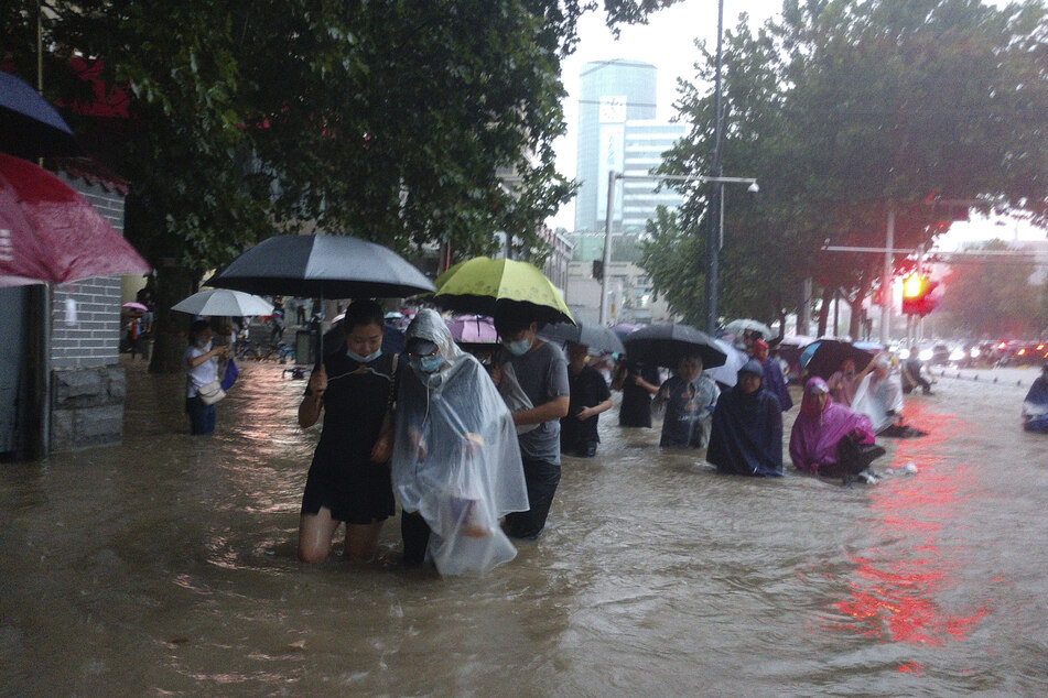 Menschen waten in der zentralchinesischen Provinz Henan durch eine überflutete Straße.