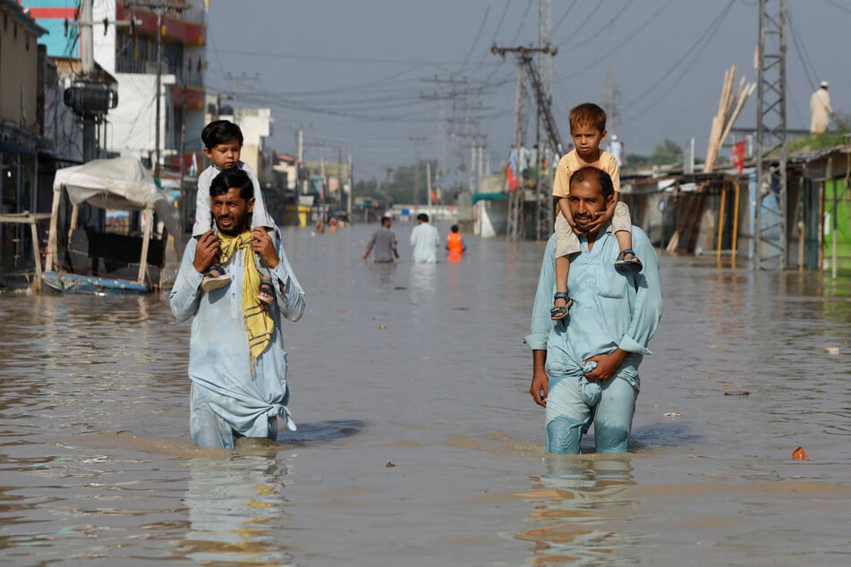 Men carry children on their shoulders and wade along a flooded road, following rains and floods during the monsoon season in Nowshera, Pakistan.