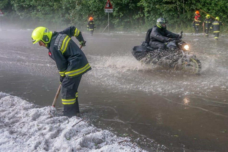Einsatzkräfte der Feuerwehr müssen nach einem Unwetter Hagelkörner beiseite schieben.