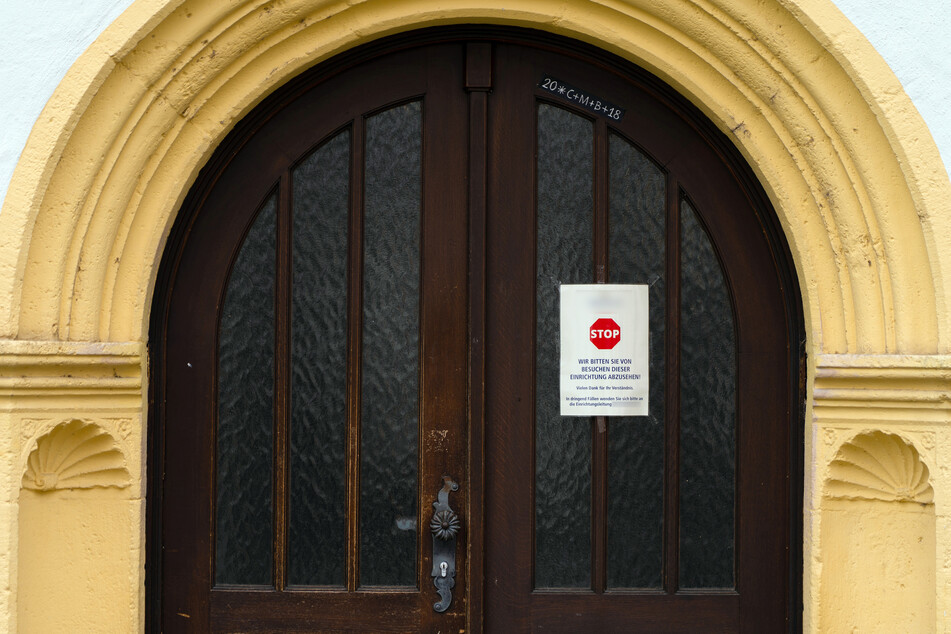 An einer Zugangstür zu einem Seniorenheim ist ein Schild angebracht, das von Besuchen dieser Einrichtung abrät.