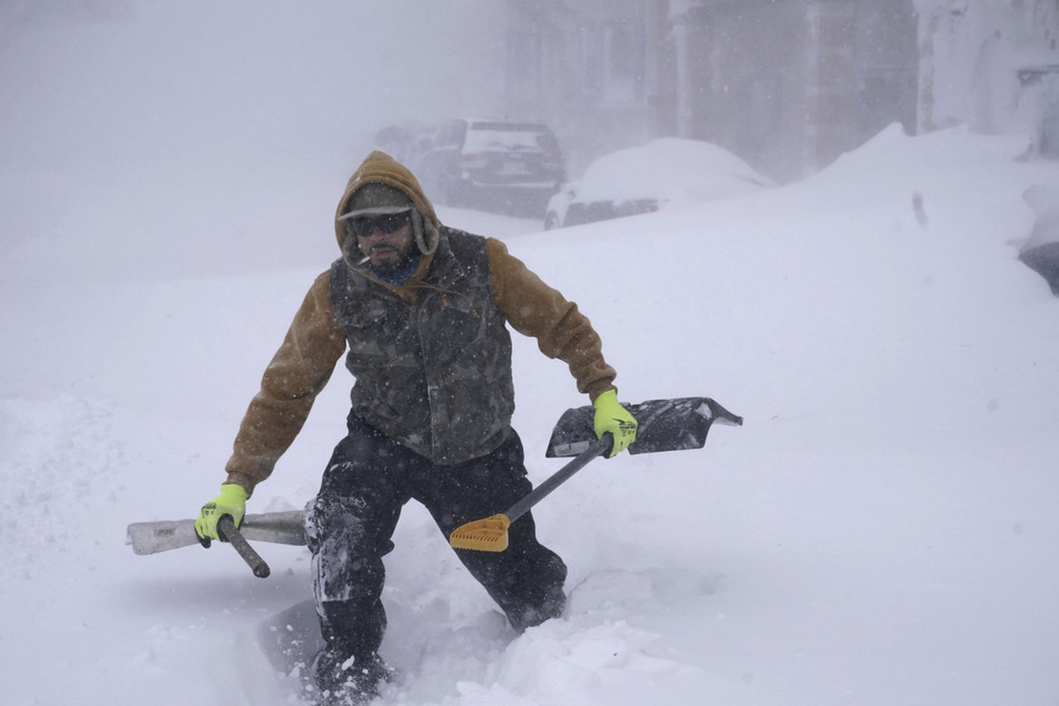 Travis Sanchez stapft mit zwei Schaufeln über eine Schneewehe, um einen gestrandeten Autofahrer in Buffalo zu helfen.