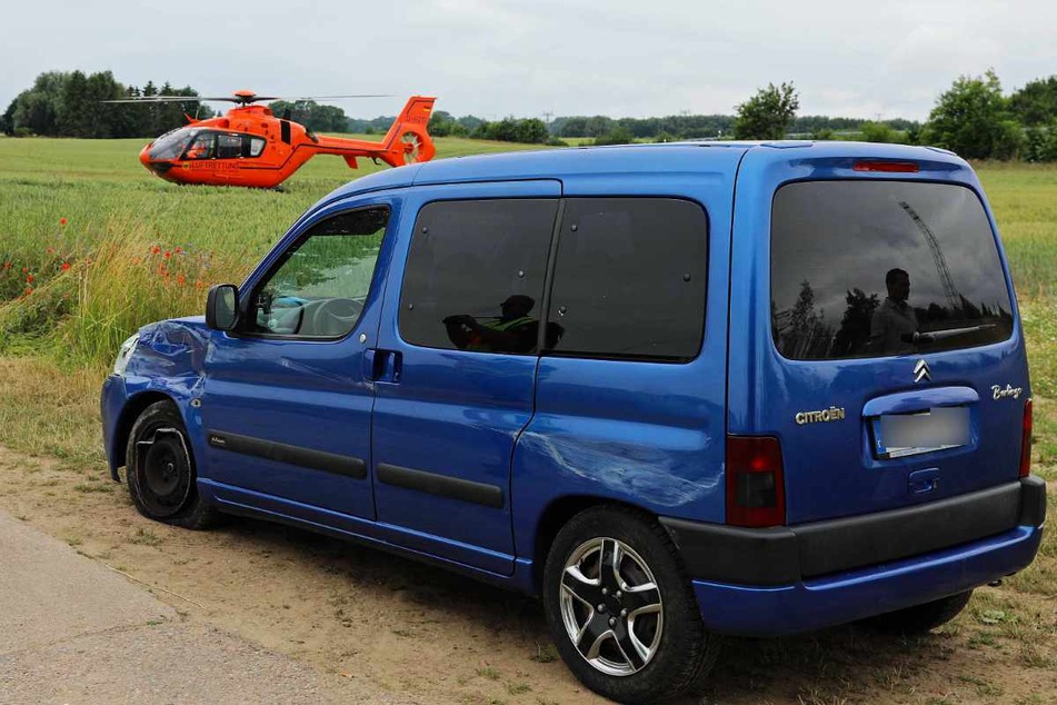 Die Spuren des Unfalls sind am Citroën deutlich zu erkennen. Im Hintergrund steht der Rettungshubschrauber auf einem Feld.