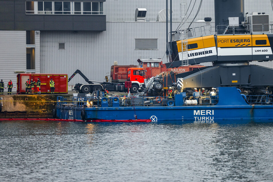 Einsatzkräfte der Feuerwehr arbeiten an der "Meri", dem Schiff, das bei der Durchfahrt der Hochbrücke in Kiel-Holtenau mit der Brücke kollidierte.