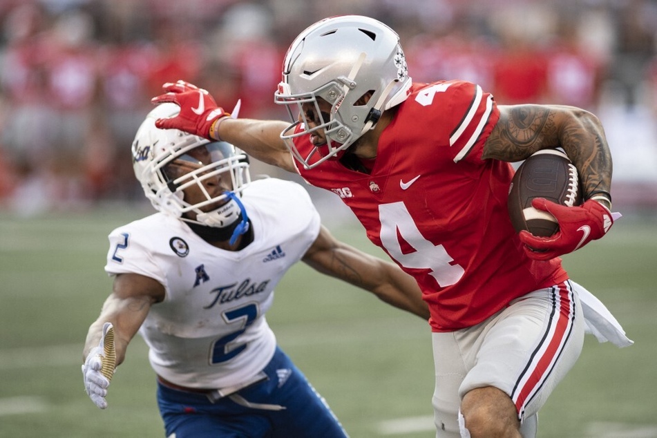 Wide receiver Julian Fleming of the Ohio State Buckeyes delivers a stiff arm to cornerback Travon Fuller of the Tulsa Golden Hurricanes.