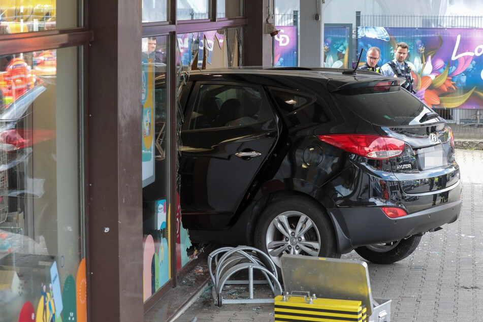 Der schwarze Hyundai blieb in der Glasfront der Drogerie in Wuppertal stecken. Polizisten sicherten die Unfallspuren.