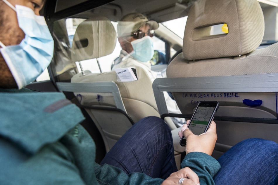Ein Fahrer vom Fahrdienst-Vermittler Uber holt in der Schweiz einen Kunden in seinem mit einer Trennwand aus Kunststoff ausgestatteten Fahrzeug ab, beide Insassen tragen Mundschutz. (Archivbild)