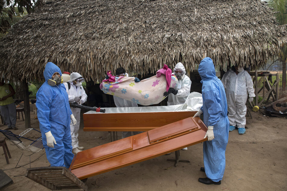 Peru, Pucallpa: Ein Regierungsteam entfernt in der indigenen Shipibo-Gemeinde von Pucallpa die Leiche einer Frau, die im Alter von 88 Jahren an den Symptomen des Coronavirus gestorben ist, aus ihrem Haus und legt sie in einen Sarg.